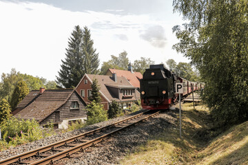 Photo of German Brocken bahn locomotive train leaving small train station on its way to the Brocken mountain in Germany on an overcast summer day. 