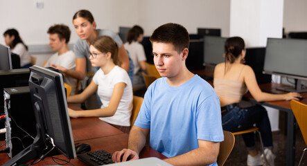 Fototapeta premium Focused teenager male student sitting at desk in college computer class, preparing for exam