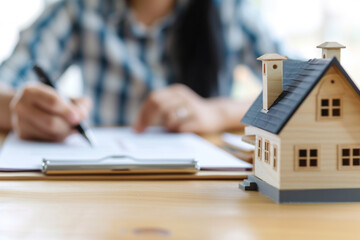 woman signs mortgage agreement in defocus,mock-up of apartment building stands next to it,concept of investing in real estate,mortgage on house,purchase and construction of housing, a mortgage loan
