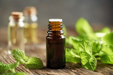 A brown bottle of aromatherapy essential oil with fresh peppermint leaves