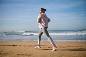 Portrait of a happy active sportswoman running along the Atlantic beach. Sports and healthy...