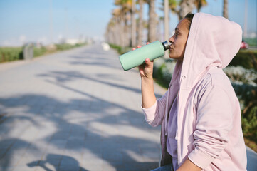 Beautiful sportswoman, female athlete drinks water to hydrate body after outdoor cardio workout....