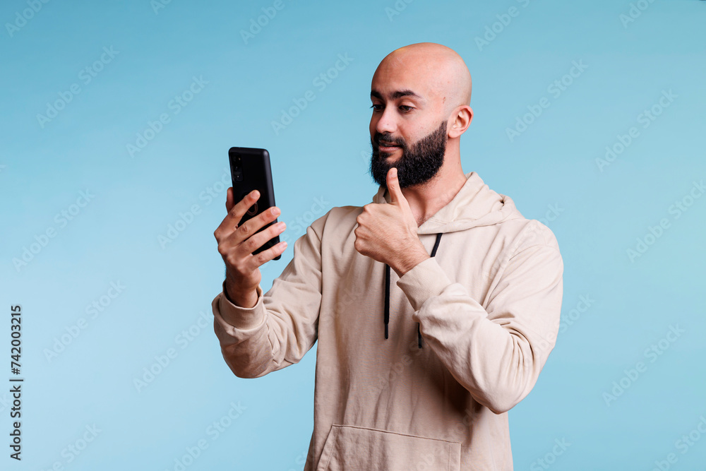 Poster young arab man showing thumb up while speaking in video call using smartphone. person making approve