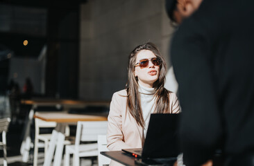 Professional woman in sunglasses using laptop at outdoor cafe.