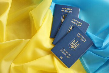 Three Ukrainian biometrical passports on folded waving flag of Ukraine country close up
