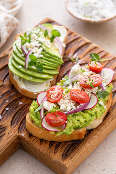 Avocado toasts on a wooden board with cream cheese, radishes and feta
