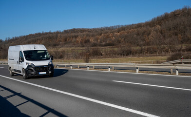 White modern delivery small shipment cargo courier van moving fast on motorway road to city urban...