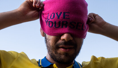 Man wearing pink cap with self love message and taking it off, sunny day