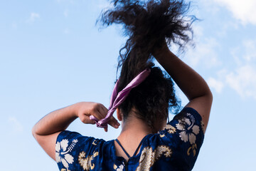 Curly girl making a bun in her hair in sunny day at summer and blue sky at background 