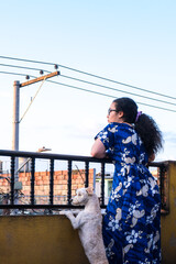 Woman standing and wearing blue dress on terrace in latin city with an electric tower in summer 