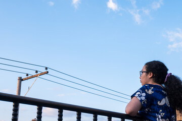 Woman standing and wearing blue dress on terrace in latin city with an electric tower in summer 