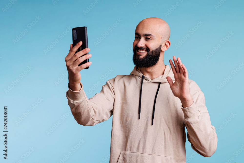 Poster smiling arab man waving hi while talking online using smartphone videocall application. friendly per