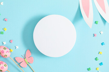 Easter holiday composition. Easter decorations, empty round platform podium, Easter eggs, colored sugar candy sprinkles, bunny isolated on pastel blue background. Easter concept. Flat lay, top view
