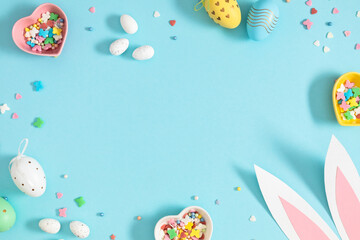 Easter holiday composition. Easter decorations, Easter eggs, colored sugar candy sprinkles, bunny isolated on pastel blue background. Easter concept. Flat lay, top view