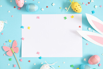 Easter party concept.  Flat lay, top view of blank sheet of paper, easter bunny ears white pink...