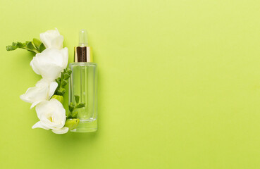 Cosmetic bottles with freesia flowers on color background, top view