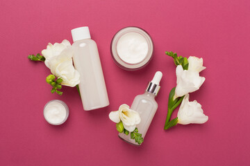 Obraz na płótnie Canvas Facial cosmetic products with freesia flowers on color background, top view