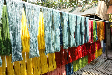 Silk threads hang in the sunlight. Rows of silk threads dyed with natural dyes hung on bamboo rods to dry in the sunshine in Thailand with copy space with selective focus.