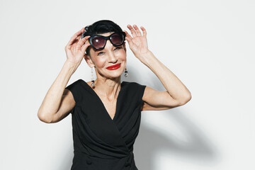 Stylish woman in black dress holding up sunglasses with red lipstick on a white background