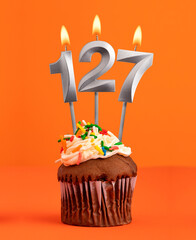 Birthday cupcake with number 127 candle - Orange color background