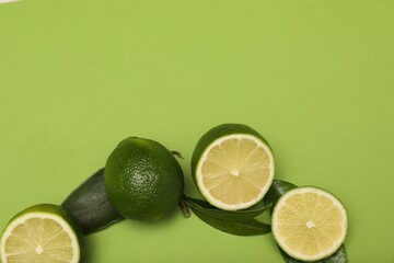 Fresh limes and leaves on green background, flat lay. Space for text