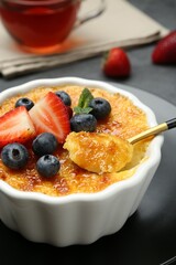 Taking delicious creme brulee with berries from bowl at grey table, closeup