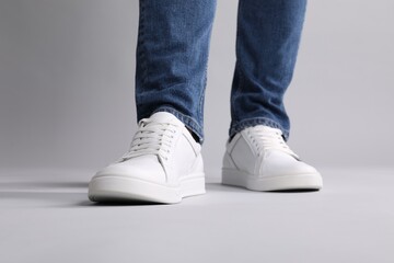 Man wearing stylish white sneakers on grey background, closeup