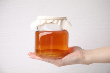 Woman holding glass jar of tasty kombucha on white background, closeup