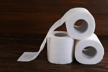 Many soft toilet paper rolls on wooden table, closeup. Space for text
