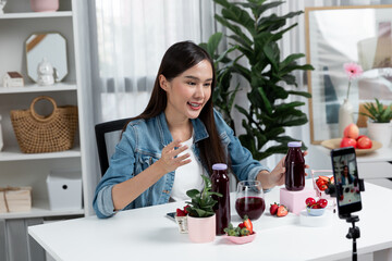 Smiling young beautiful Asian reviewing tasty mixed strawberry and cherry juice detox drinks,...