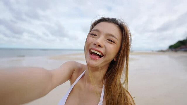 4K Happy Asian woman travel nature ocean on summer holiday vacation. Point of view Attractive girl in bikini enjoy outdoor lifestyle using mobile phone vlogging at tropical island beach in sunny day.