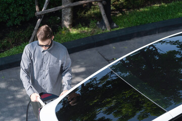 Young man travel with EV electric car charging in green sustainable city outdoor garden in summer...