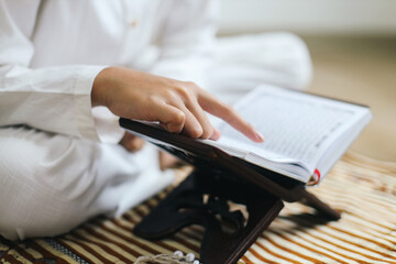 Young moslem man sitting on prayer mat reading Quran