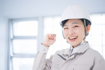 メインビジュアルにも！作業着を着たカメラ目線のヘルメットを被る女性　ガッツポーズでやる気のイメージのクローズアップ