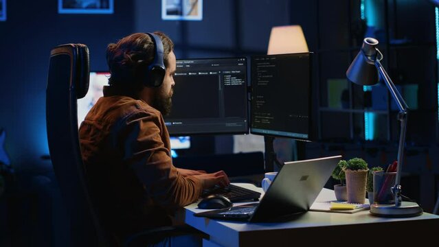 Engineer typing code in apartment office, using javascript programming language to develop software application. It admin using multimonitor desktop setup and notebook to finish tasks, camera A
