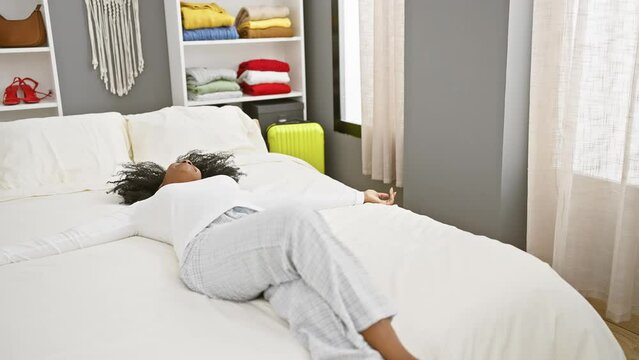 African american woman relaxing on a white bed in a modern bedroom, showcasing a carefree and comfortable lifestyle.