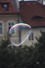 A shimmering, iridescent soap bubble floats delicately in the air before a picturesque house.