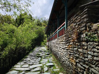 A narrow stone path winds past a sturdy stone building, creating a harmonious connection between nature and architecture.