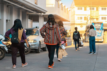 Back view of Asian elderly woman traveler in casual clothes walks down a street with travel bag in...