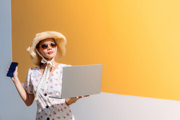 Presenter concept of Asian businesswoman and hotel tourist, 20-30 years old, holding a smartphone and relaxing, wearing a hat and dress, with sunglasses, holding a laptop during the holiday season.