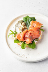 Homemade bagel sandwich with smoked salmon, cream cheese, capers and spinach for healthy breakfast on white kitchen background for breakfast