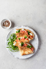 Crepes or thin pancakes with smoked salmon, soft cheese and spinach on a plate top view isolated on gray textured background. Pancake day, Maslenitsa