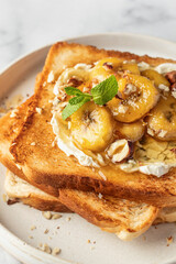 Sweet toast with cream cheese, caramelized banana, nuts and honey in white plate on marble background close up