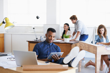 Obraz premium Workplace, laptop and tablet with man as architect with blueprints in office of creative company with colleagues. Male person, relax and working with technology, connection and internet for projects