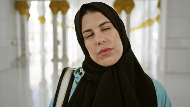 A thoughtful woman wearing a hijab stands in a mosque with elegant islamic architecture in abu dhabi.