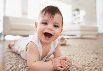 Happy, baby portrait and tummy time on floor, laugh and play in living room. Teething, child development and growth learning to crawl by laying on stomach, curious kid in white vest for at home fun - obrazy, fototapety, plakaty