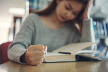 Stressed woman student with clenched fist reading a book at table, closeup