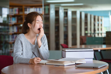 Young asian woman yawning while reading a book in library.