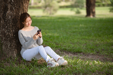 Young asian woman using smartphone while sitting on the ground in city park.