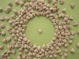 Extruded heart-shaped bran is poured onto a green background forming a circular void space for the text. Spikelets of wheat. The concept of proper snacking, proper nutrition and weight loss